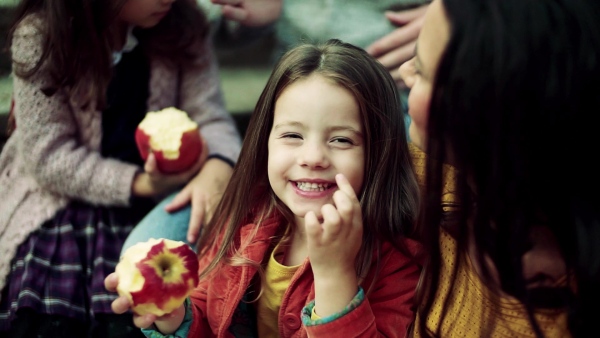 A portrait of small girl with family having picnic in autumn nature, eating apple. Slow motion.