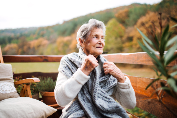 An elderly senior woman sitting outdoors on a terrace in on a sunny day in autumn.