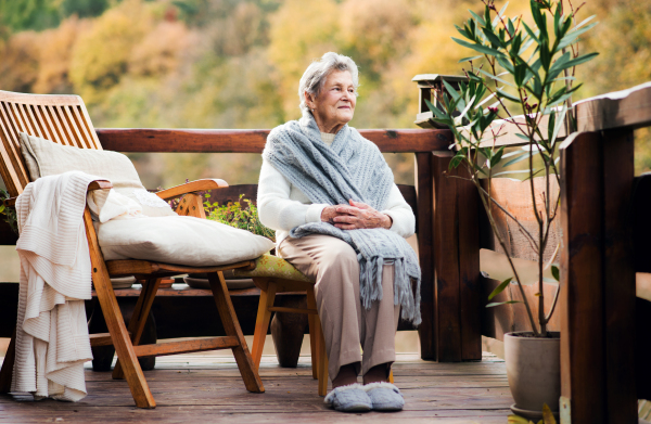 An elderly senior woman sitting outdoors on a terrace in on a sunny day in autumn.