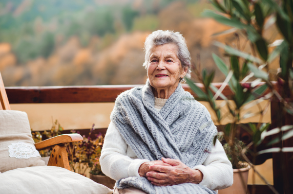 An elderly senior woman sitting outdoors on a terrace in on a sunny day in autumn.