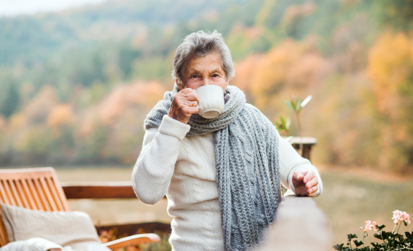 An elderly woman drinking coffee outdoors on a terrace in on a sunny day in autumn.