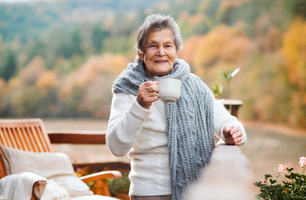 An elderly senior woman standing outdoors on a terrace in on a sunny day in autumn.