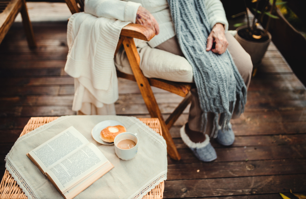 A midsection view of elderly woman with a cup of coffee and book outdoors on a terrace in autumn.