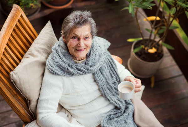 A top view of an elderly woman with a cup of tea or coffee sitting outdoors on a terrace on a sunny day in autumn.