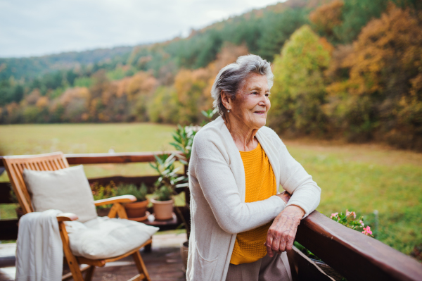 An elderly senior woman standing outdoors on a terrace on a sunny day in autumn.