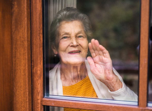 A happy elderly woman standing by the window, looking out. Shot through glass.