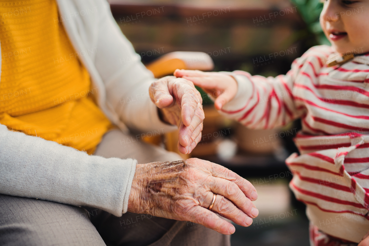 A midsection of elderly woman with a toddler great-grandchild sitting outdoors on a terrace on a sunny day in autumn.