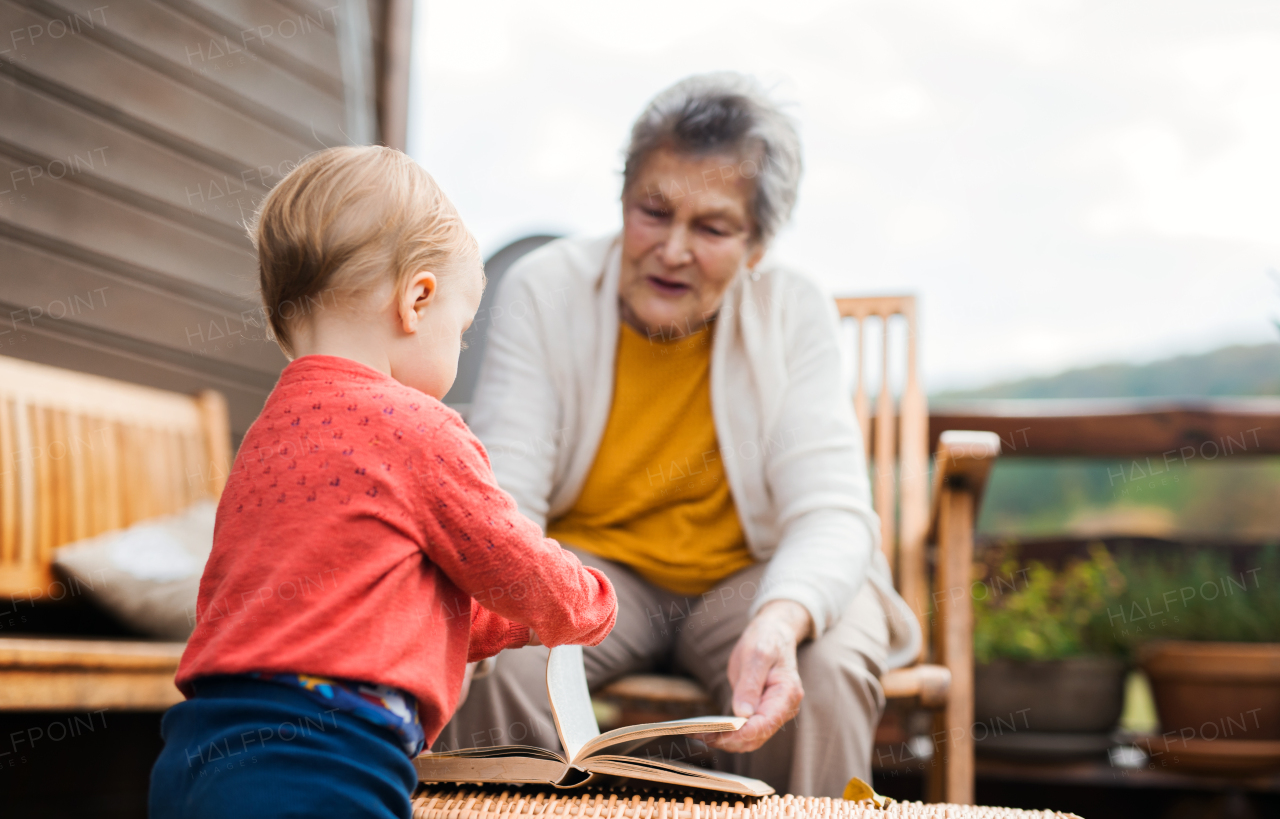 An elderly woman with a toddler great-grandchild on a terrace on a sunny day in autumn.