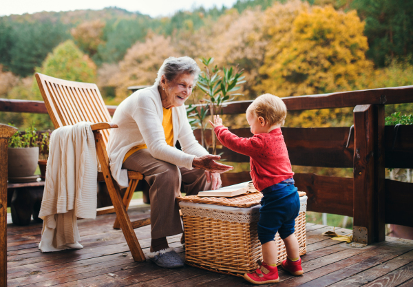 An elderly woman with a toddler great-grandchild on a terrace on a sunny day in autumn.