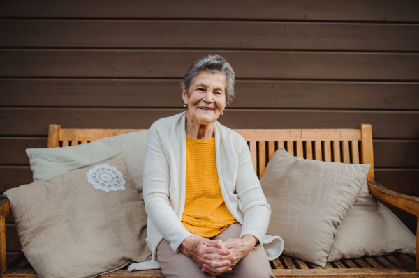 An elderly senior woman sitting outdoors on a terrace in on a sunny day in autumn.