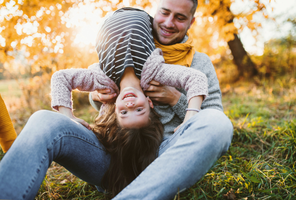 A young father holding a small daughter in autumn nature, having fun.