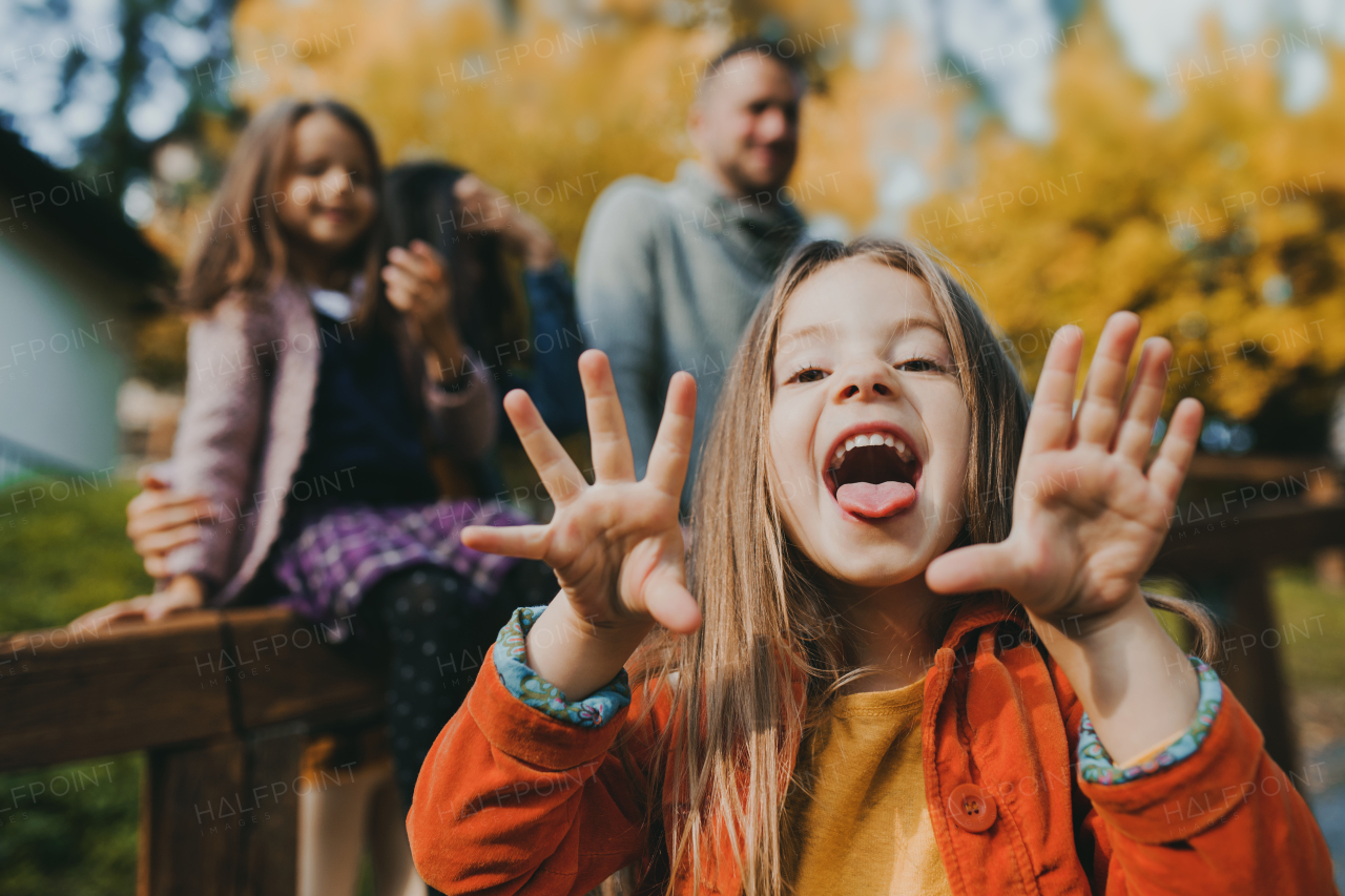 A portrait of happy small girl with her family in town in autumn, sticking out tongue.