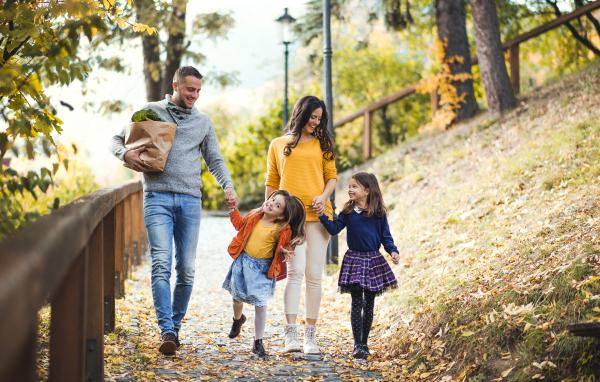 A young family with two children walking down a path in park in autumn.