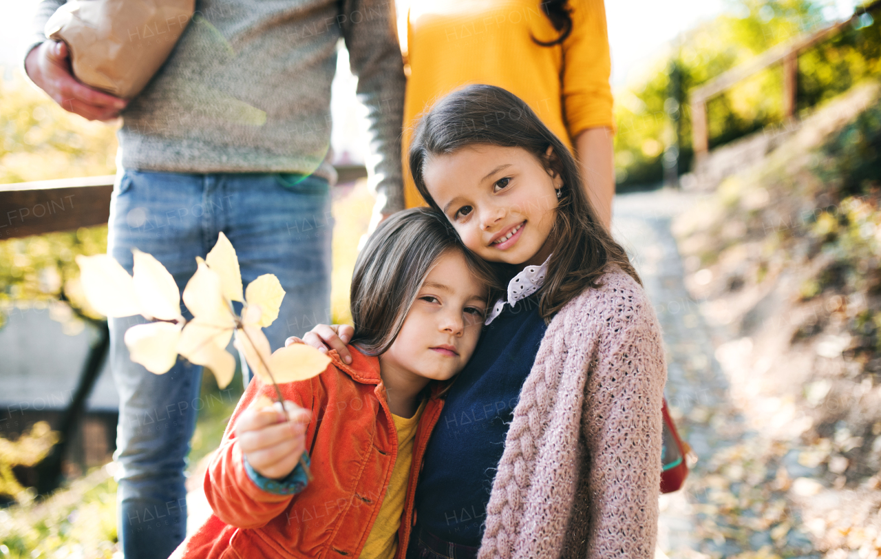 A young family with two children walking down a path in park in autumn.