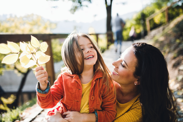 A portrait of young mother with a small daughter sitting on a ground in autumn nature.