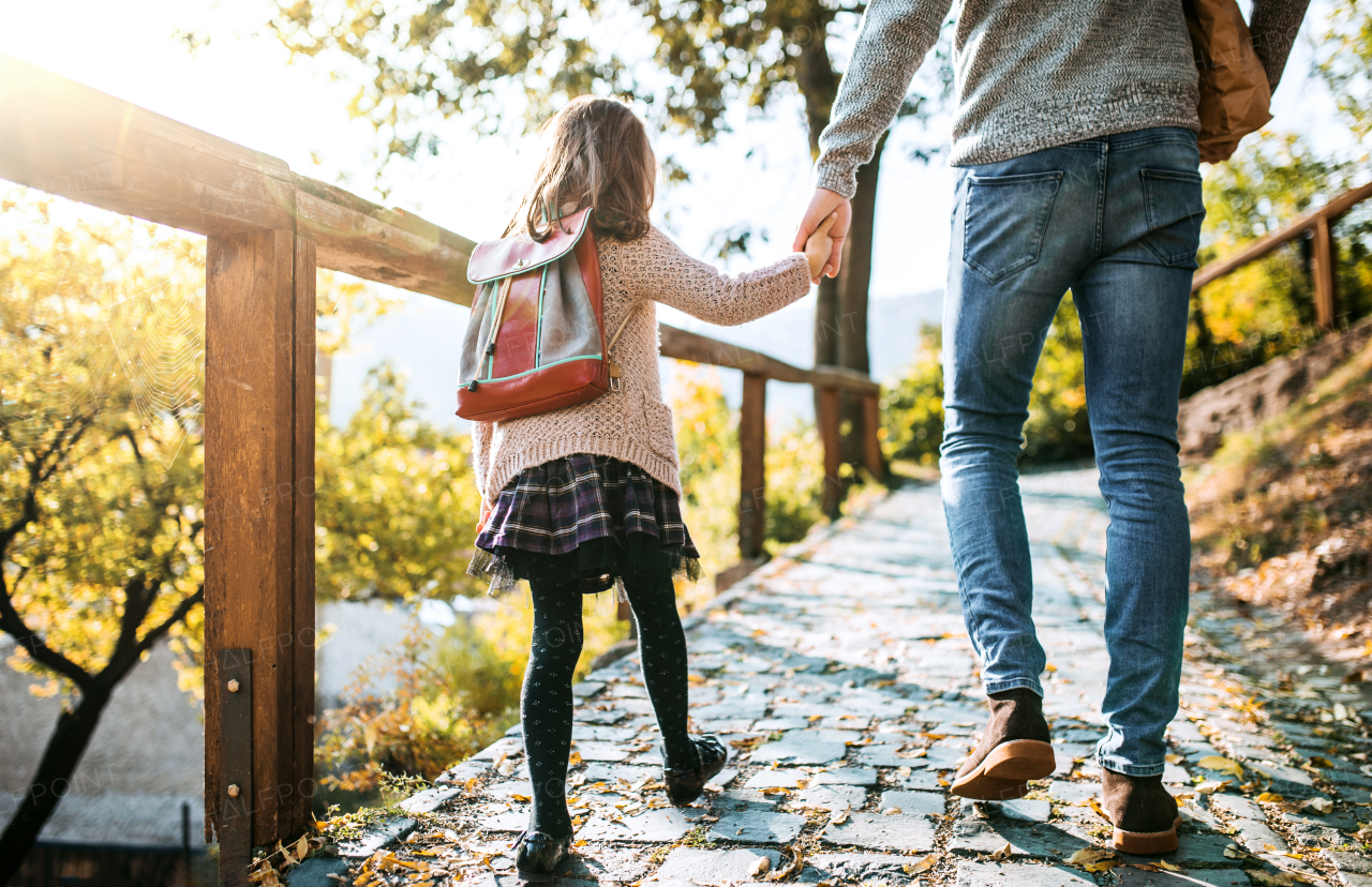 A rear view of unrecognizable young father walking with a small daughter in town in autumn.