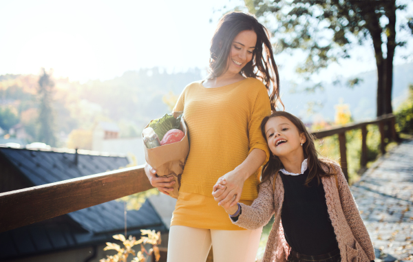 A young mother with small daughter walking in town in autumn, carrying shopping.