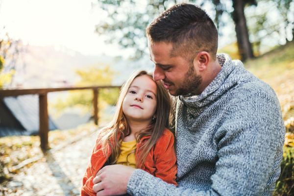 A young father holding a small daughter in autumn nature, sitting.