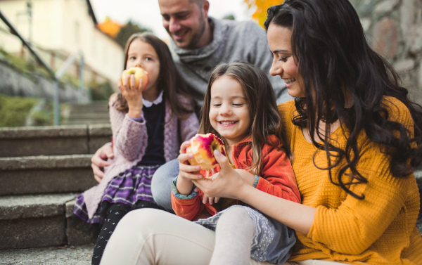 A portrait of young family with two small children in town in autumn, eating apples.