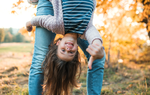 An unrecognizable father holding a small daughter upside down in autumn nature.