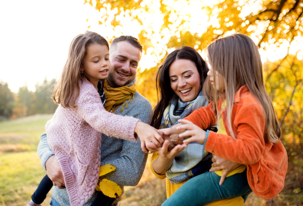 A portrait of happy young family with two small children holding nuts in autumn nature.