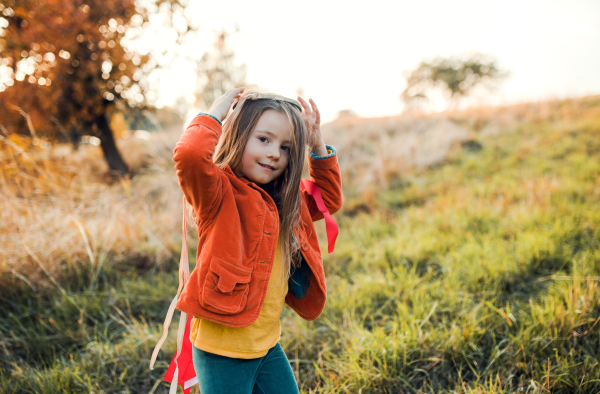 A happy small girl playing with a rainbow hand kite in autumn nature at sunset. Copy space.