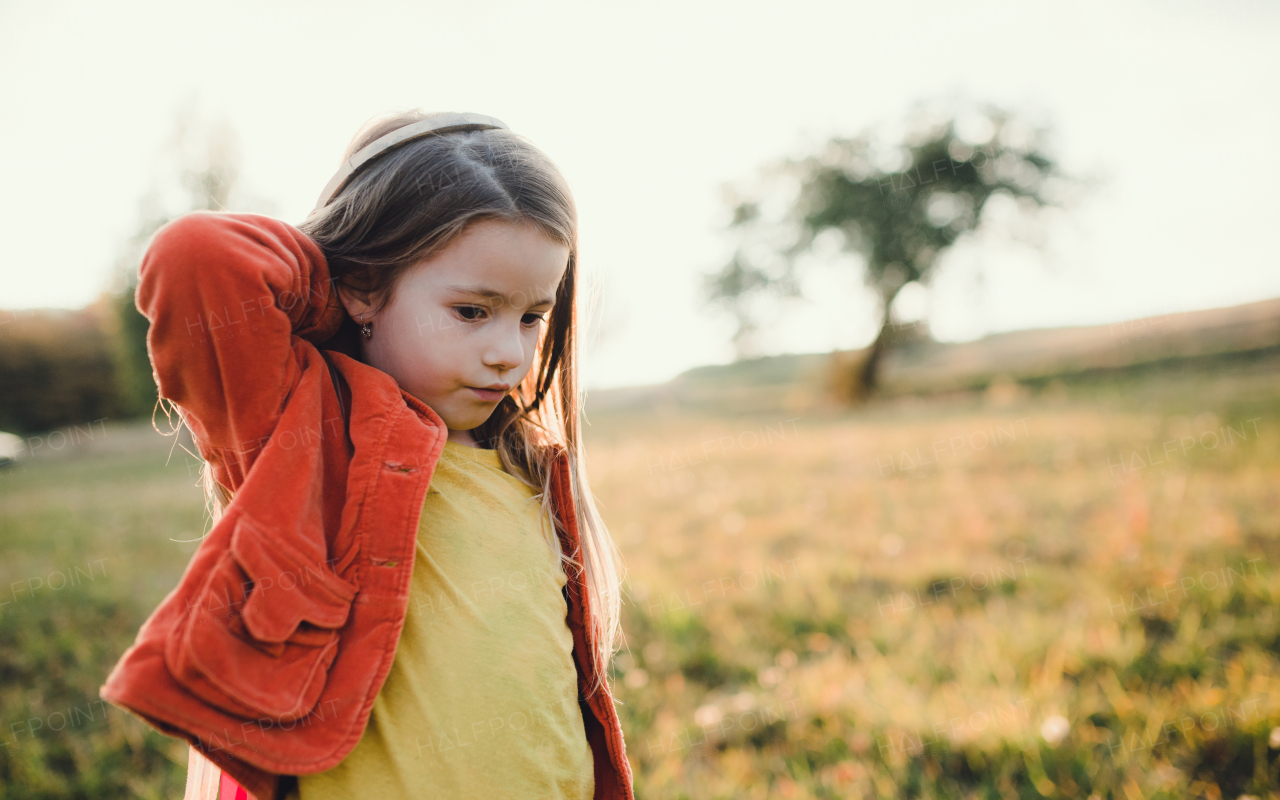 A small girl walking in autumn nature at sunset, playing. Copy space.