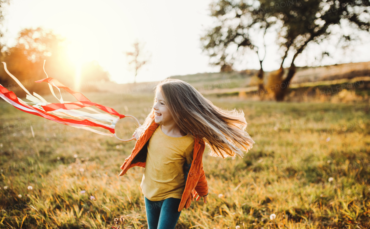 A happy small girl playing with a rainbow hand kite in autumn nature at sunset.