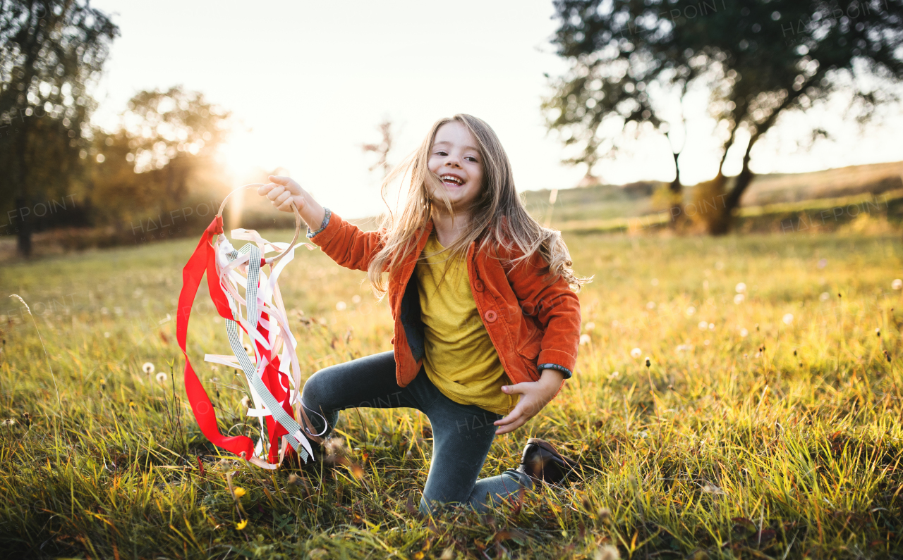 A happy small girl playing with a rainbow hand kite in autumn nature at sunset.