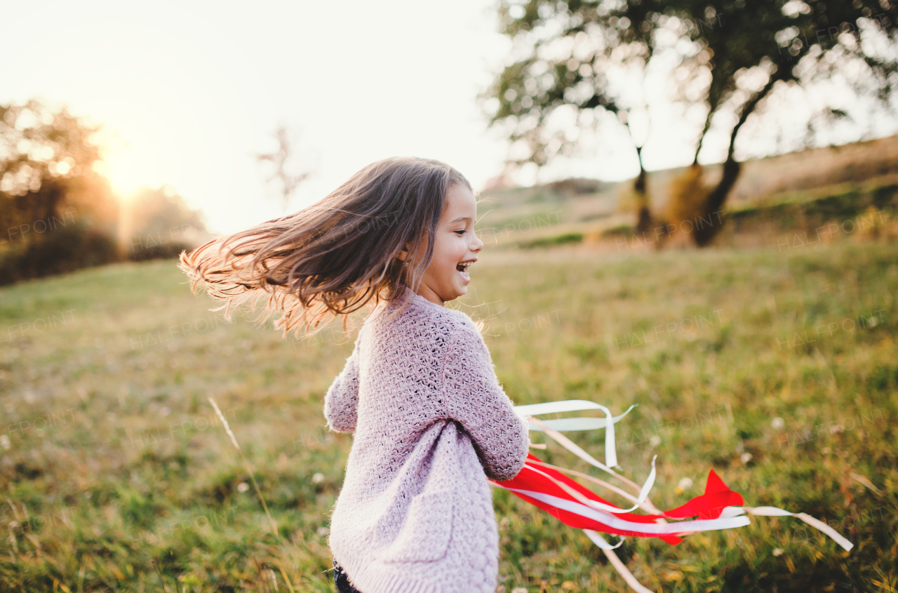 A happy small girl playing with a rainbow hand kite in autumn nature at sunset.