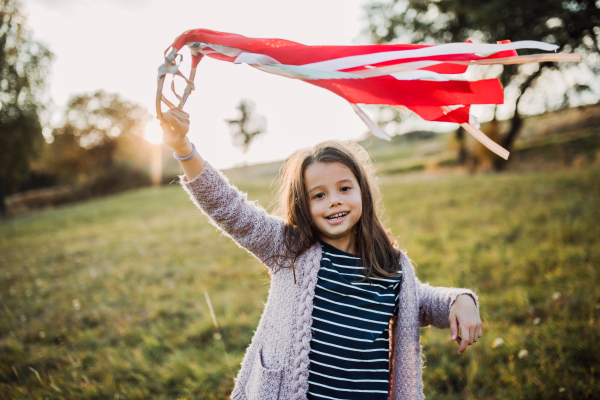 A happy small girl playing with a rainbow hand kite in autumn nature at sunset.