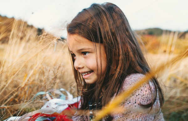 A happy small girl playing with a rainbow hand kite in autumn nature.