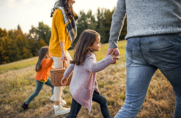 A midsection view of happy young family with two small children walking in autumn nature.