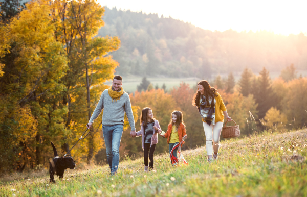 A young family with two small children and a black dog on a walk in autumn nature.