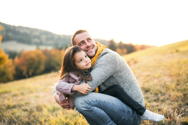 A young father holding a small daughter in autumn nature, having fun.