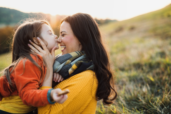 A portrait of young mother with a small daughter sitting on a ground in autumn nature at sunset.