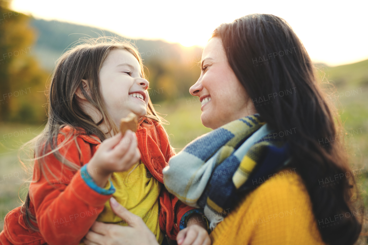 A portrait of young mother with a small daughter sitting on a ground in autumn nature at sunset.