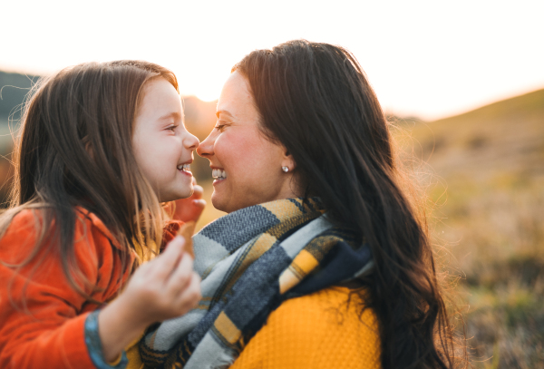 A portrait of young mother with a small daughter sitting on a ground in autumn nature at sunset.