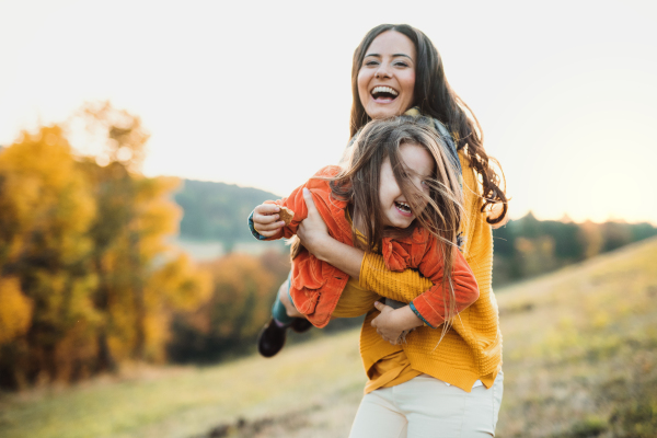 A portrait of young mother with a small daughter in autumn nature at sunset, having fun.