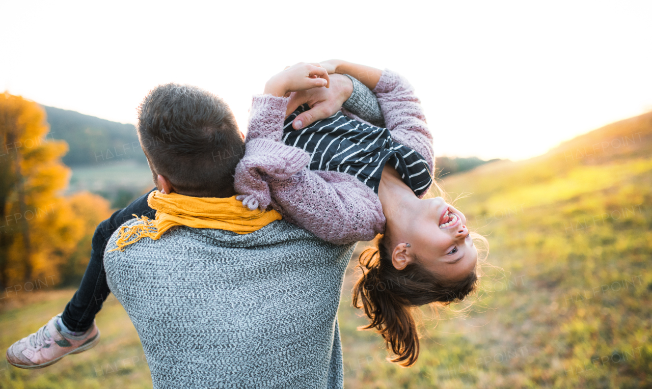 A rear view of young father holding a small daughter in autumn nature, having fun.