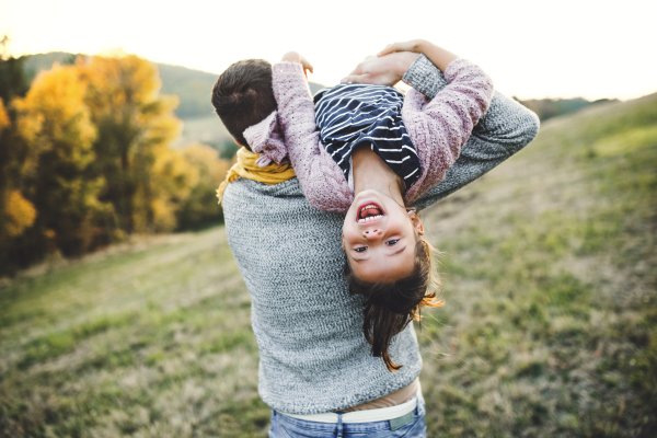 A rear view of young father holding a small daughter in autumn nature, having fun.