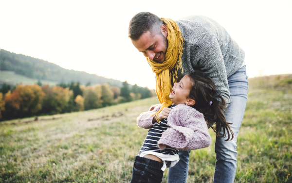 A rear view of young father holding a small daughter in autumn nature, having fun.