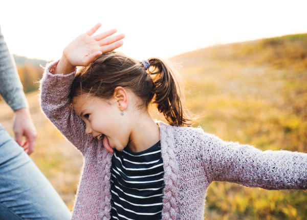 A happy small girl with unrecognizable father in autumn nature, having fun.