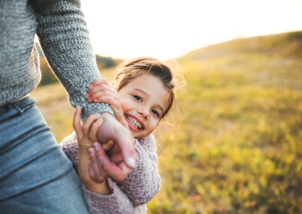 A happy small girl with unrecognizable father in autumn nature, having fun.