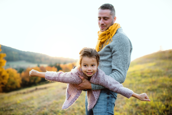 A young father having fun with a happy small daughter in autumn nature.