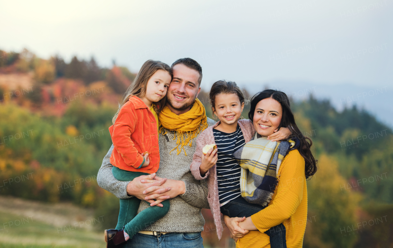 A portrait of happy young family with two small children standing in autumn nature.