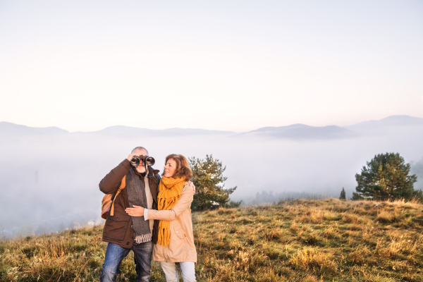 Active senior couple on a walk in a beautiful autumn nature. Old man looking through binoculars.