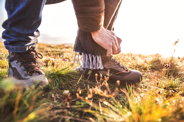 Active senior man on a walk in a beautiful autumn nature. Unrecognizable man tying his shoelaces. Close up.