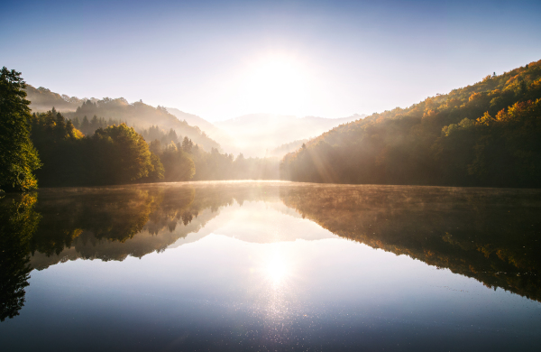 Sunrise on the lake in nature. Autumn colourful forest reflected in water.