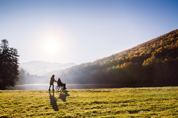 Active senior couple on a walk in a beautiful autumn nature. A woman and man in a wheelchair by the lake in the early morning.